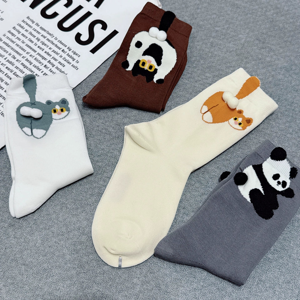 Four pairs of novelty socks arranged on a gray textured surface, each featuring a different cartoon animal face: a white rabbit, a brown cow, an orange fox, and a black-and-white panda. A printed paper is partially visible in the top left corner.